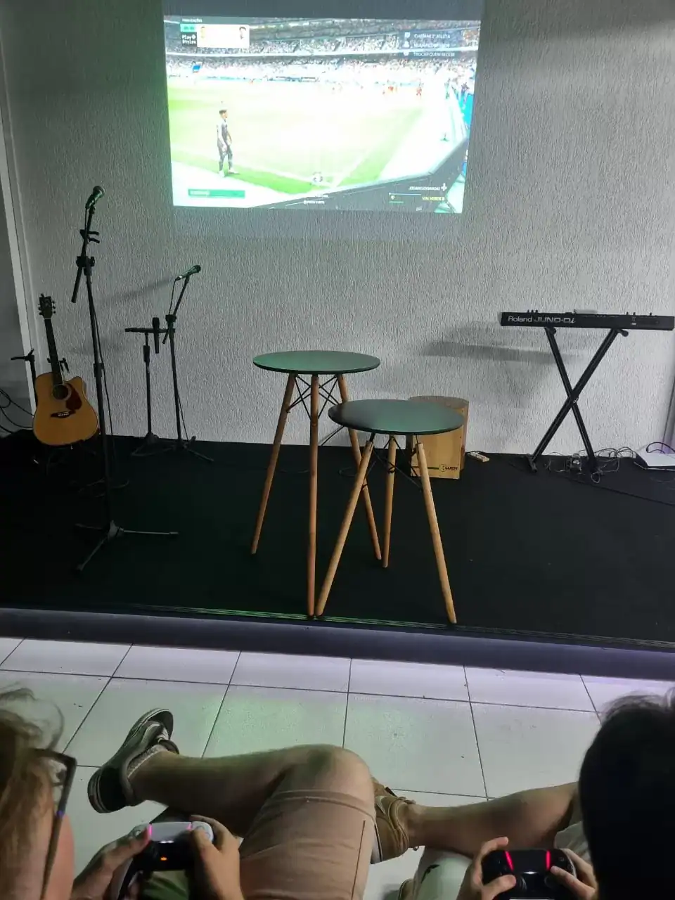 Natus gaming setup with guitar, microphones, and electronic keyboard on stage for live music and gaming events in a casual indoor environment.