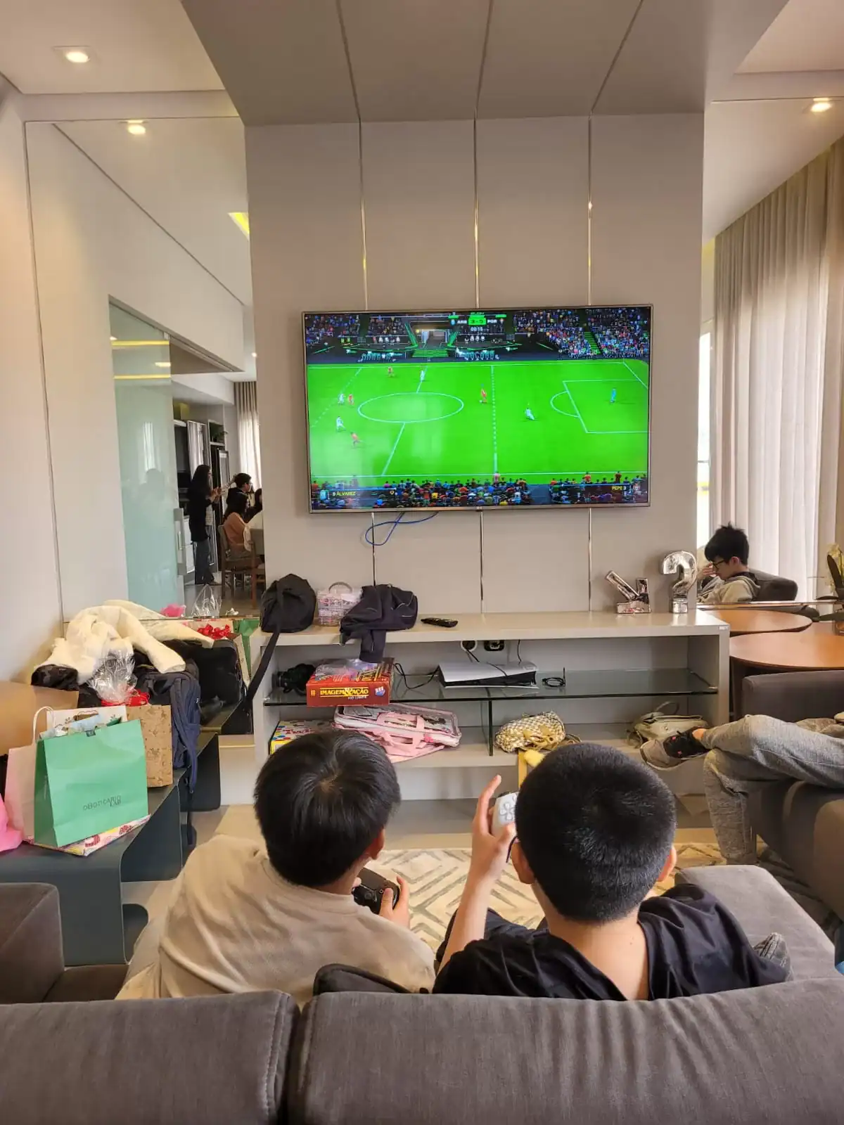Esporte ao vivo na televisão com pessoas jogando videogame de futebol em um ambiente de lazer.